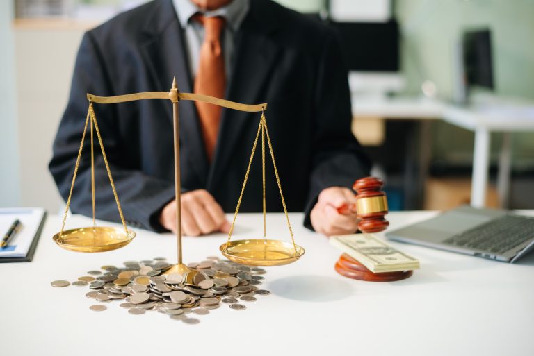 Lawyer with gavel and scales of justice on desk with coins.