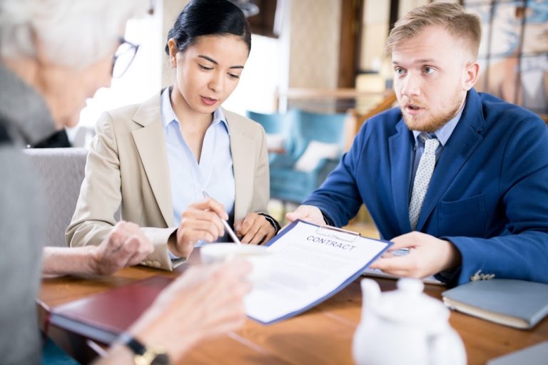 Two professionals discussing a business contract with an elderly individual at a wooden table.