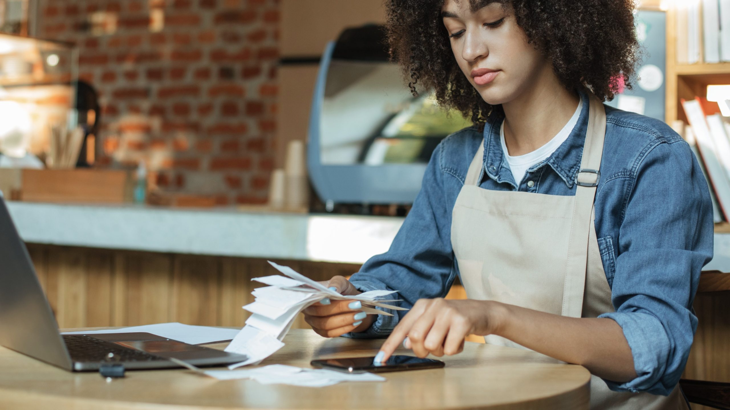 Woman sorting receipts using smartphone at cafe